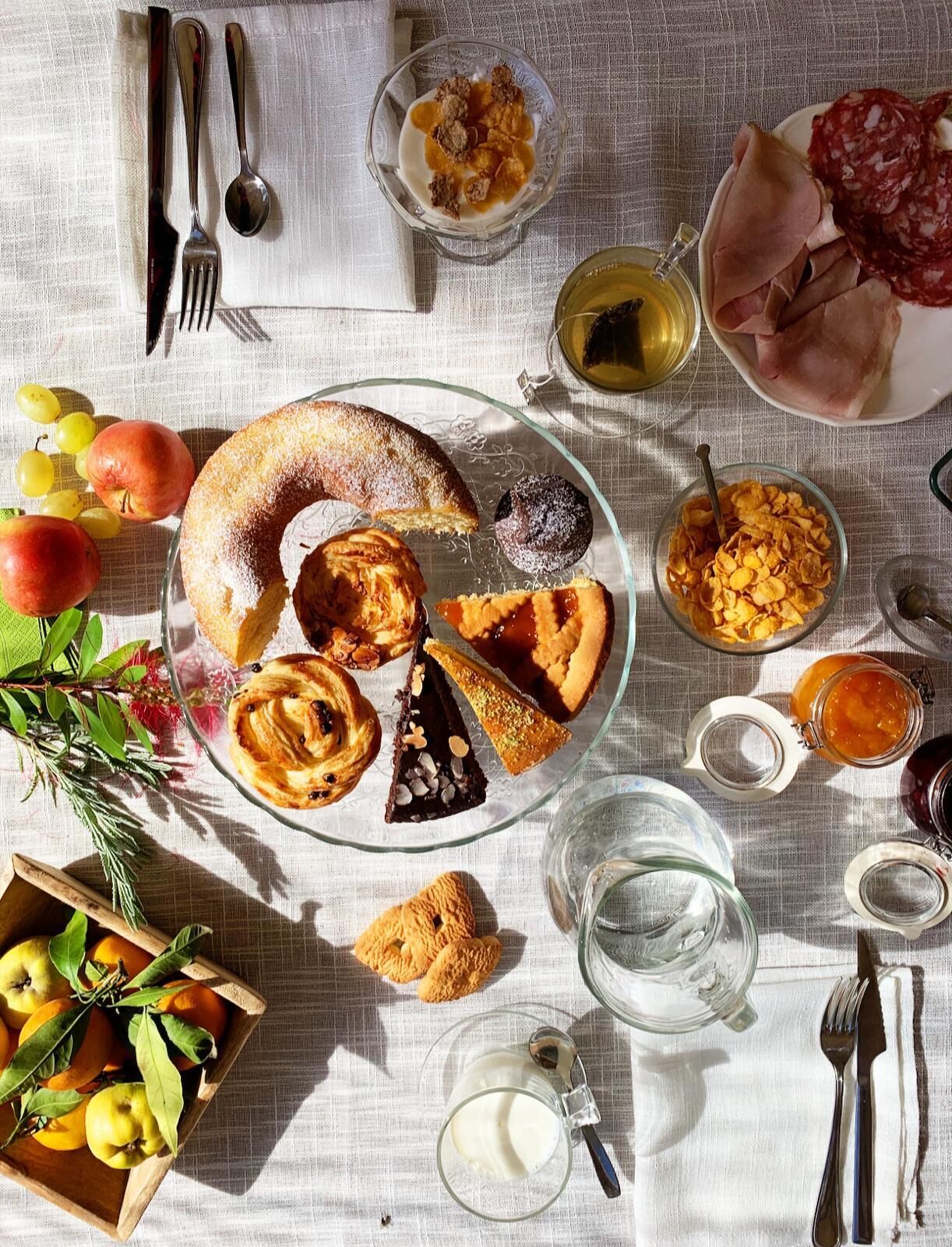 Uma mesa posta com diversos alimentos e bebidas, incluindo doces, frutas e acompanhamentos.