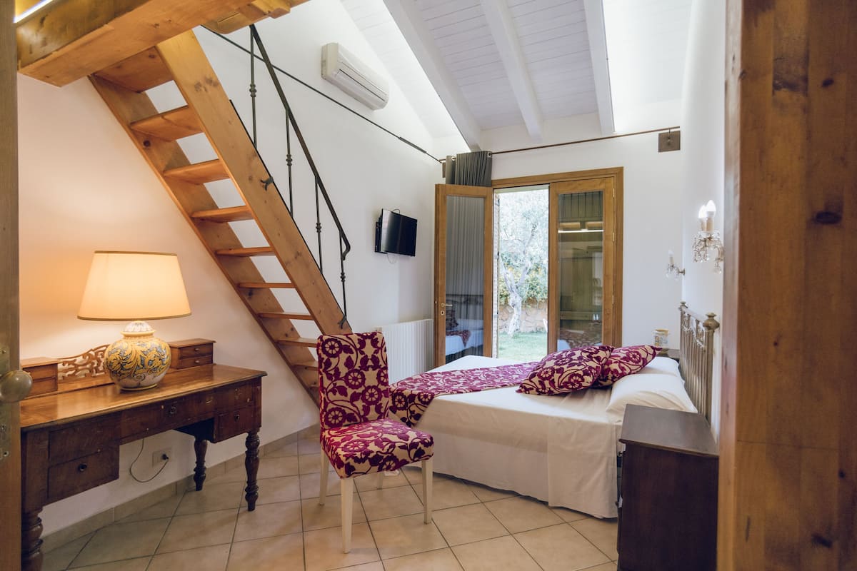 A bedroom with a bed, a chair, a desk, and a staircase.