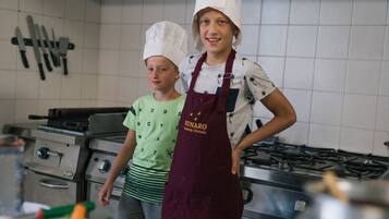 A kitchen with two individuals wearing chef hats and aprons, a stove, and various cooking utensils.