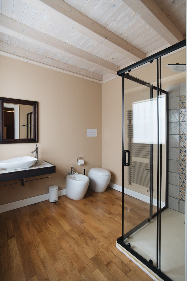 A modern bathroom with a wooden floor, a white sink, a toilet, and a glass shower enclosure. - Agriresort Leano (Piazza Armerina)