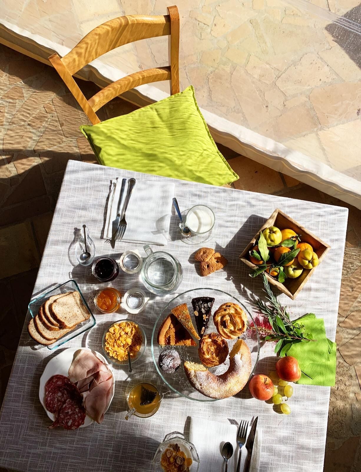 A table set outdoors with a variety of food items, including bread, pastries, and fruits.