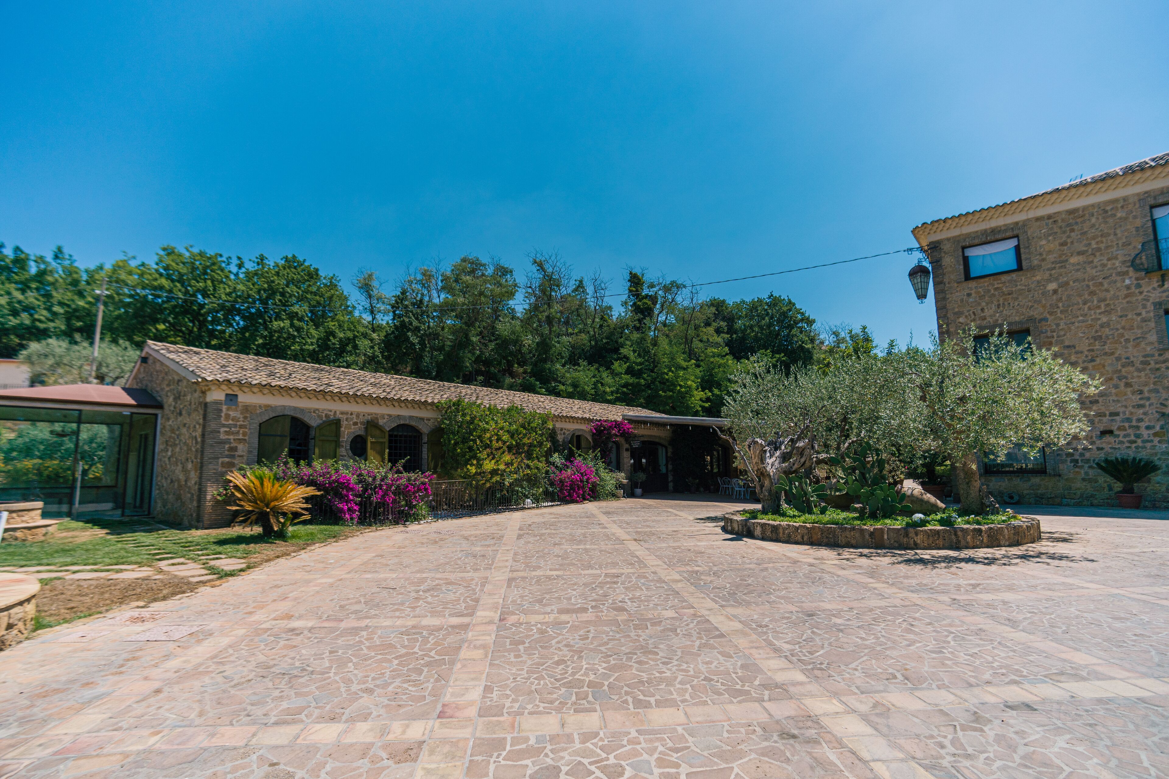 A courtyard with stone flooring, a building with a tiled roof, and surrounding greenery.