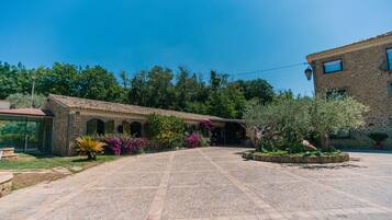 A courtyard with stone flooring, a building with a tiled roof, and surrounding greenery.