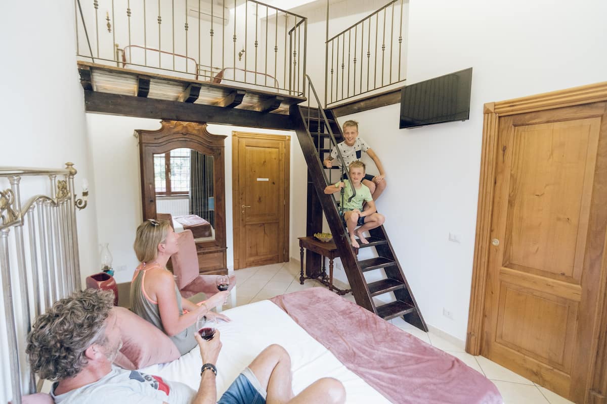 A bedroom with a bed, a wooden door, a staircase, and a mirror.