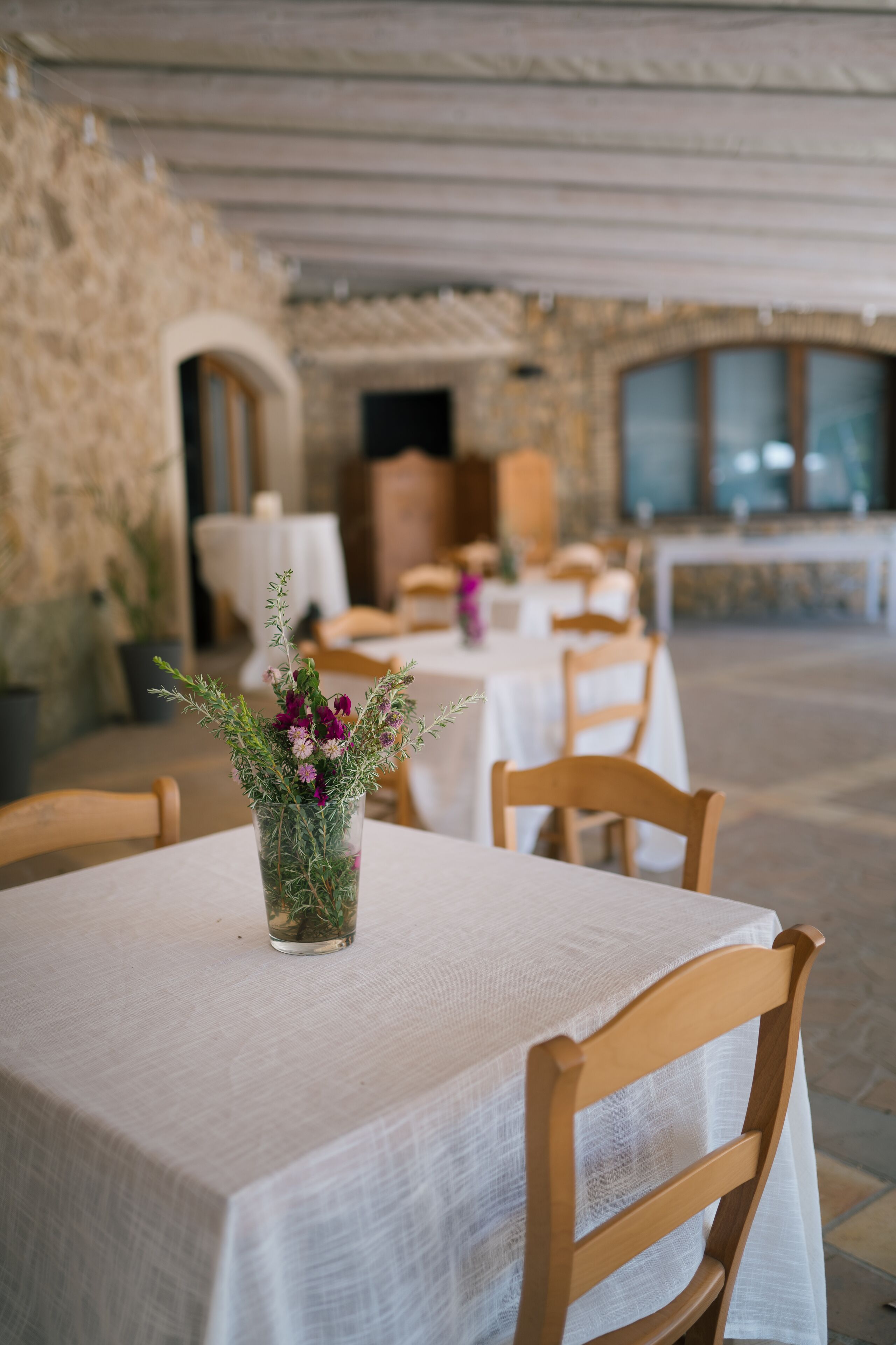 Ein Restaurant mit Tischen, die mit weißen Tischdecken bedeckt sind, hölzernen Stühlen und einem Blumenstrauß auf einem Tisch.