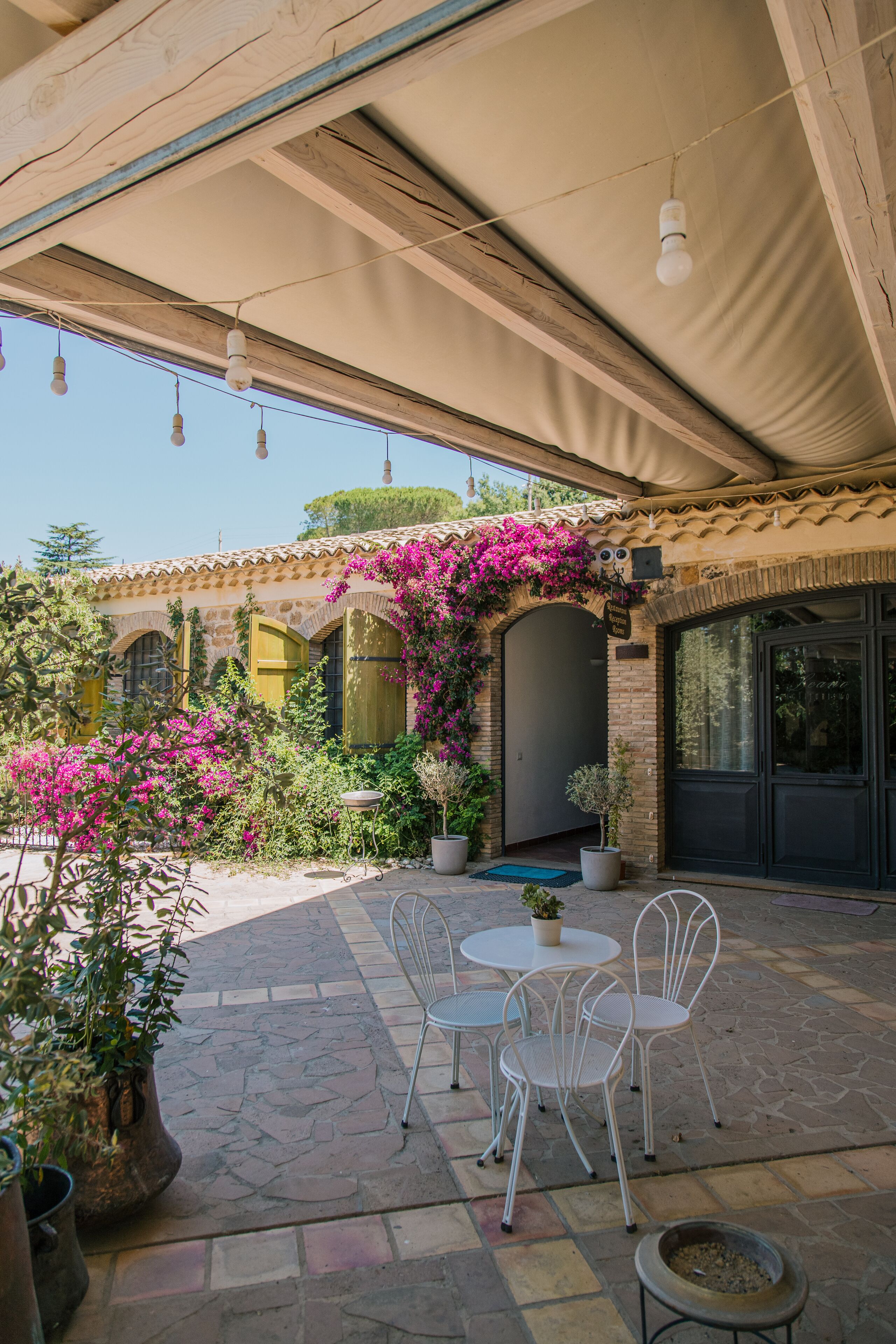 An outdoor patio with stone flooring, white metal chairs, and potted plants.