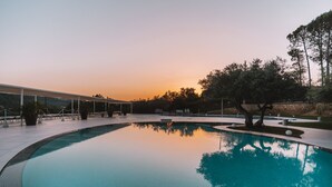 A swimming pool with a curved edge, surrounded by a paved area with benches and a covered walkway. - Agriresort Leano (Piazza Armerina)