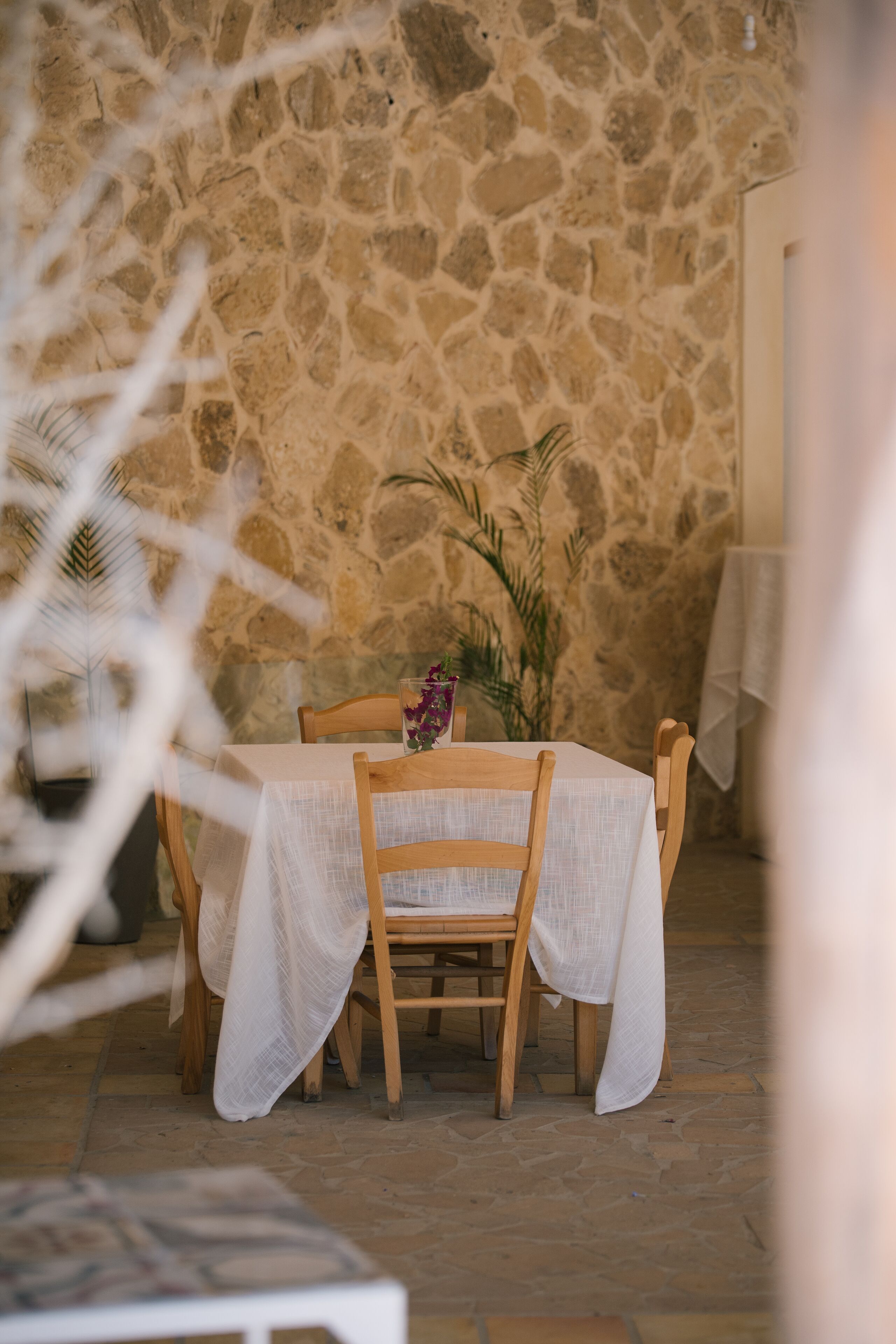 Un mur de pierres, une table recouverte d’une nappe blanche et des chaises en bois.