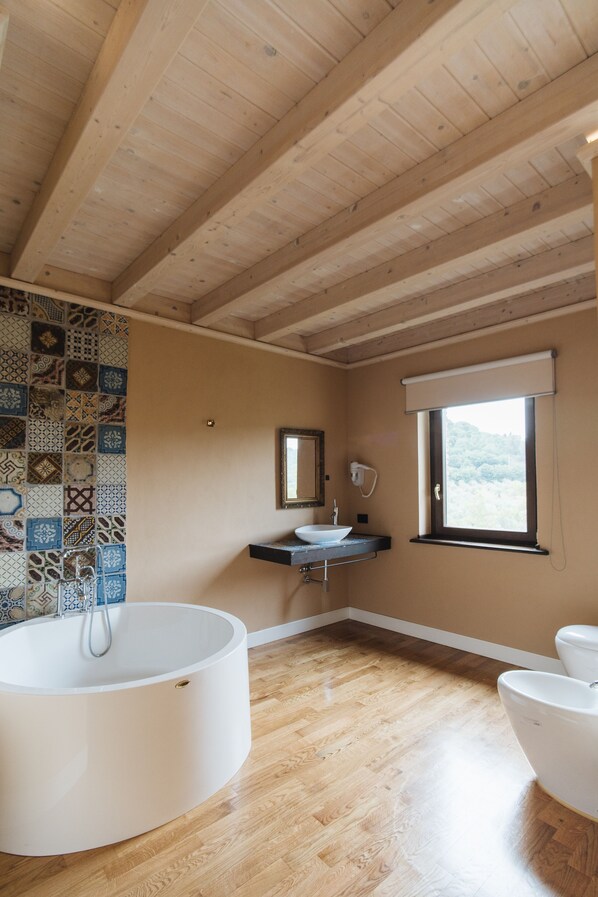 Un baño con techo de madera, una bañera, un lavabo, un inodoro y un ventanal con vistas.