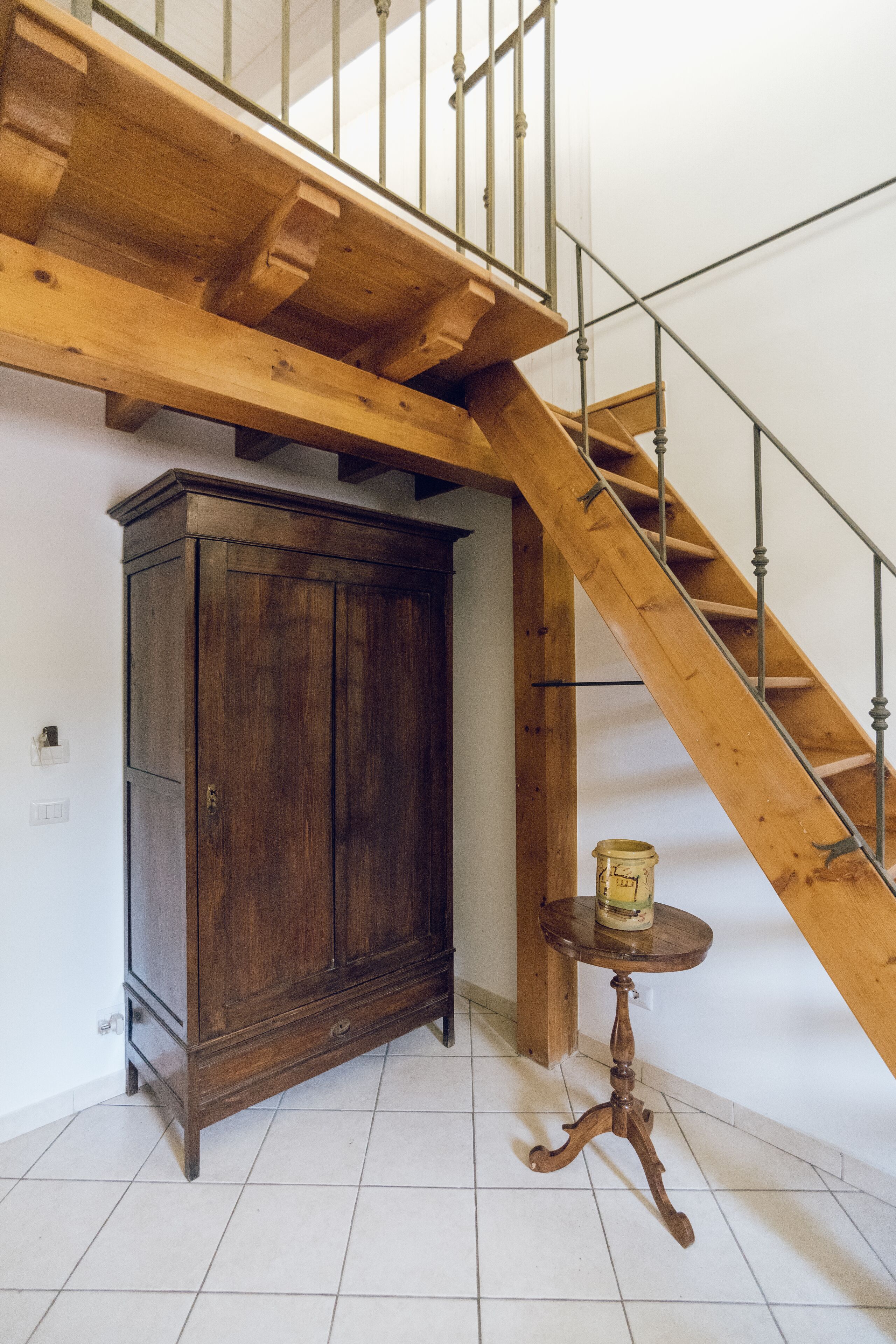 A wooden staircase with a metal railing, a wooden cabinet, and a small round table with a can on it.