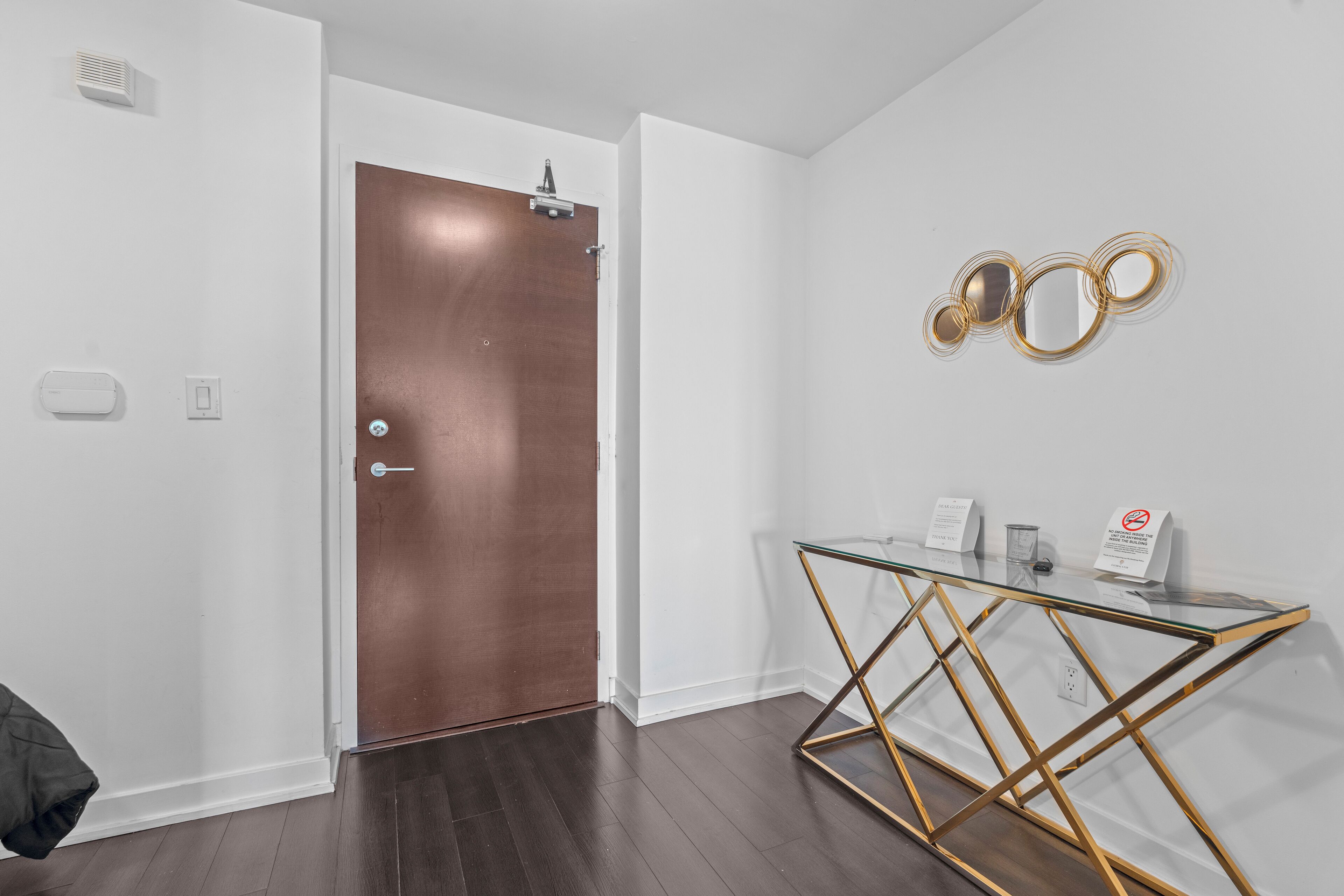 A modern interior with a wooden door, a glass table with gold legs, and a wall-mounted circular mirror.