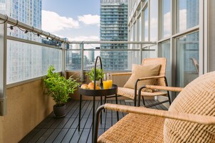 Een balkon met rieten stoelen, een tafeltje met een plant en een glas jus d'orange, en uitzicht op de stad.