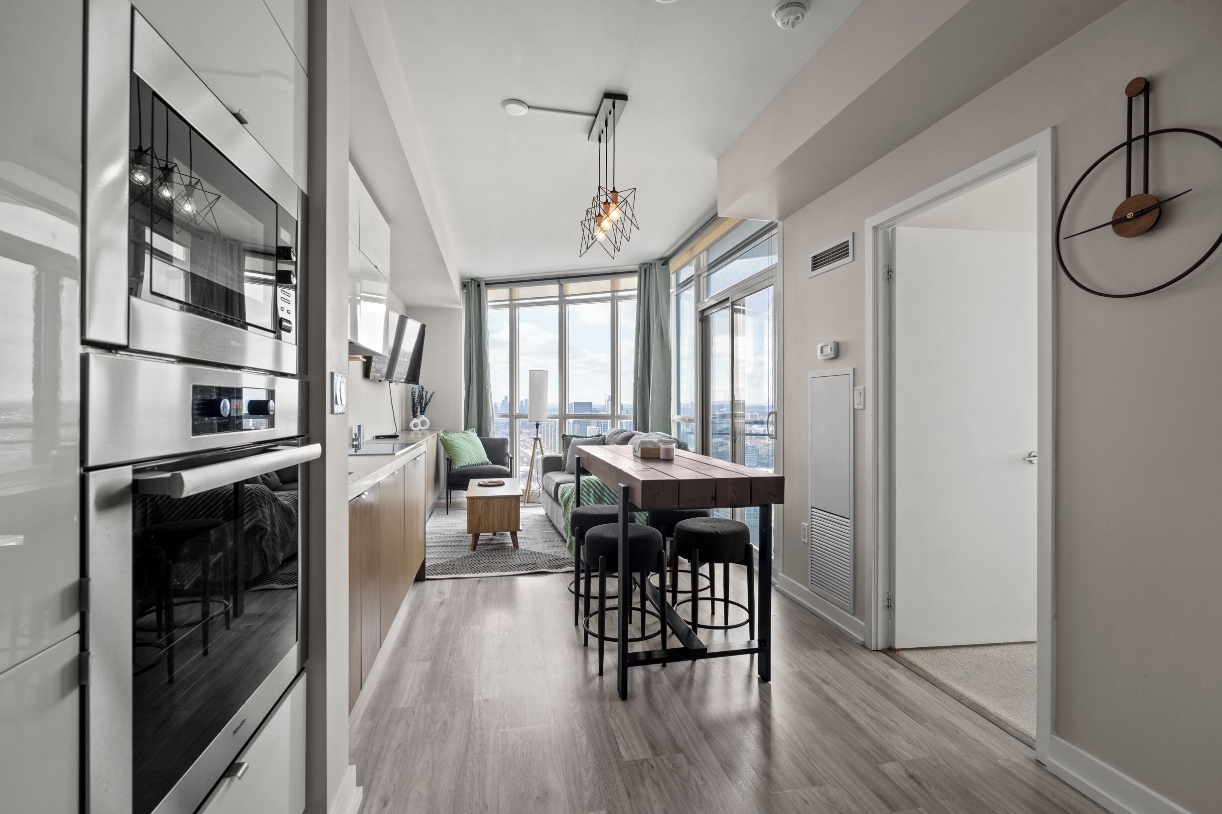 Eine moderne Küche mit Edelstahlgeräten, eine Essecke mit Holztisch und Barhocker sowie große Fenster mit Blick auf die Stadt.