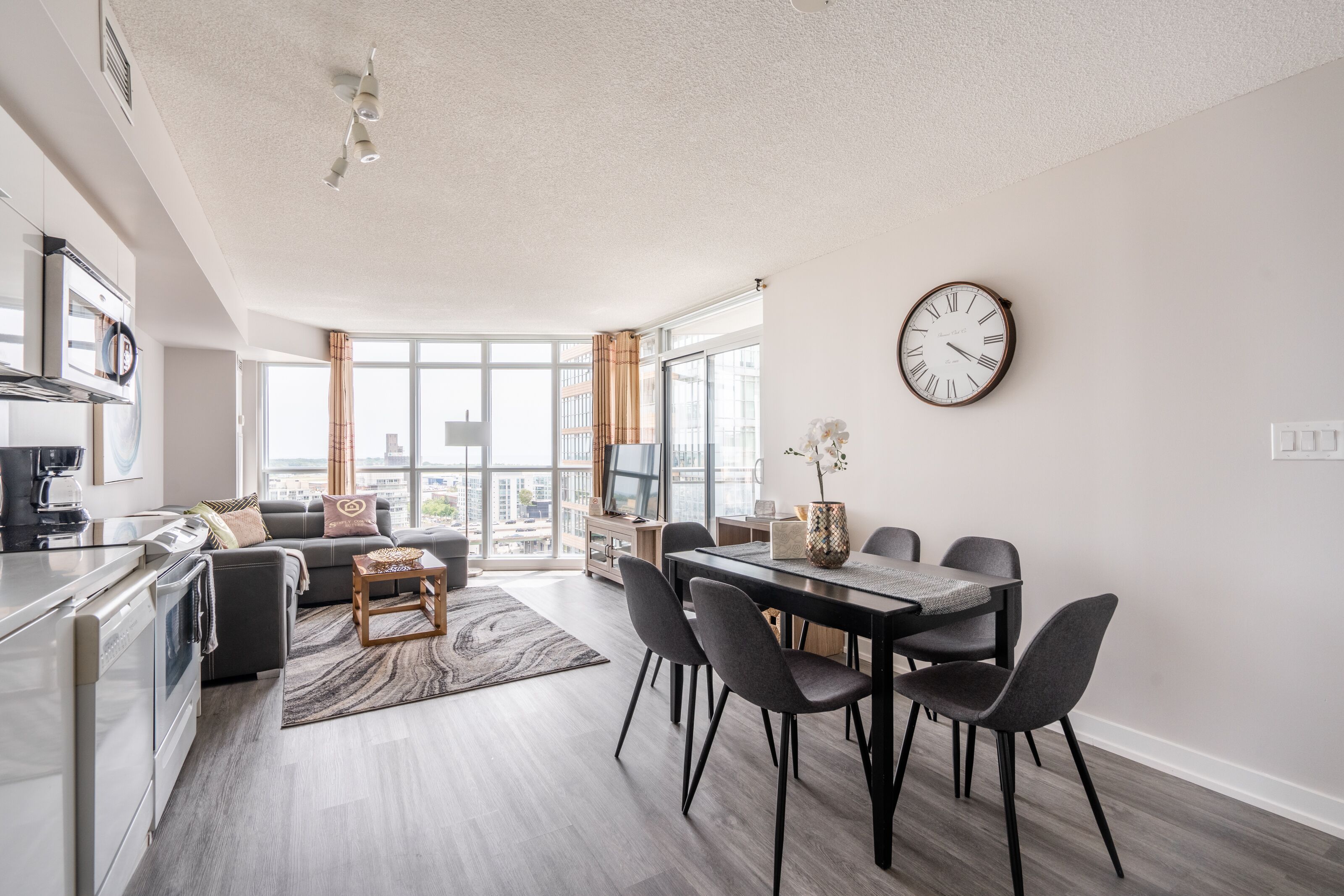 Un appartement moderne comprenant une cuisine, un coin repas et un salon. Il est doté de grandes fenêtres, d'une table à manger avec des chaises et d'un canapé.