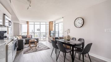 Un appartement moderne comprenant une cuisine, un coin repas et un salon. Il est doté de grandes fenêtres, d'une table à manger avec des chaises et d'un canapé.
