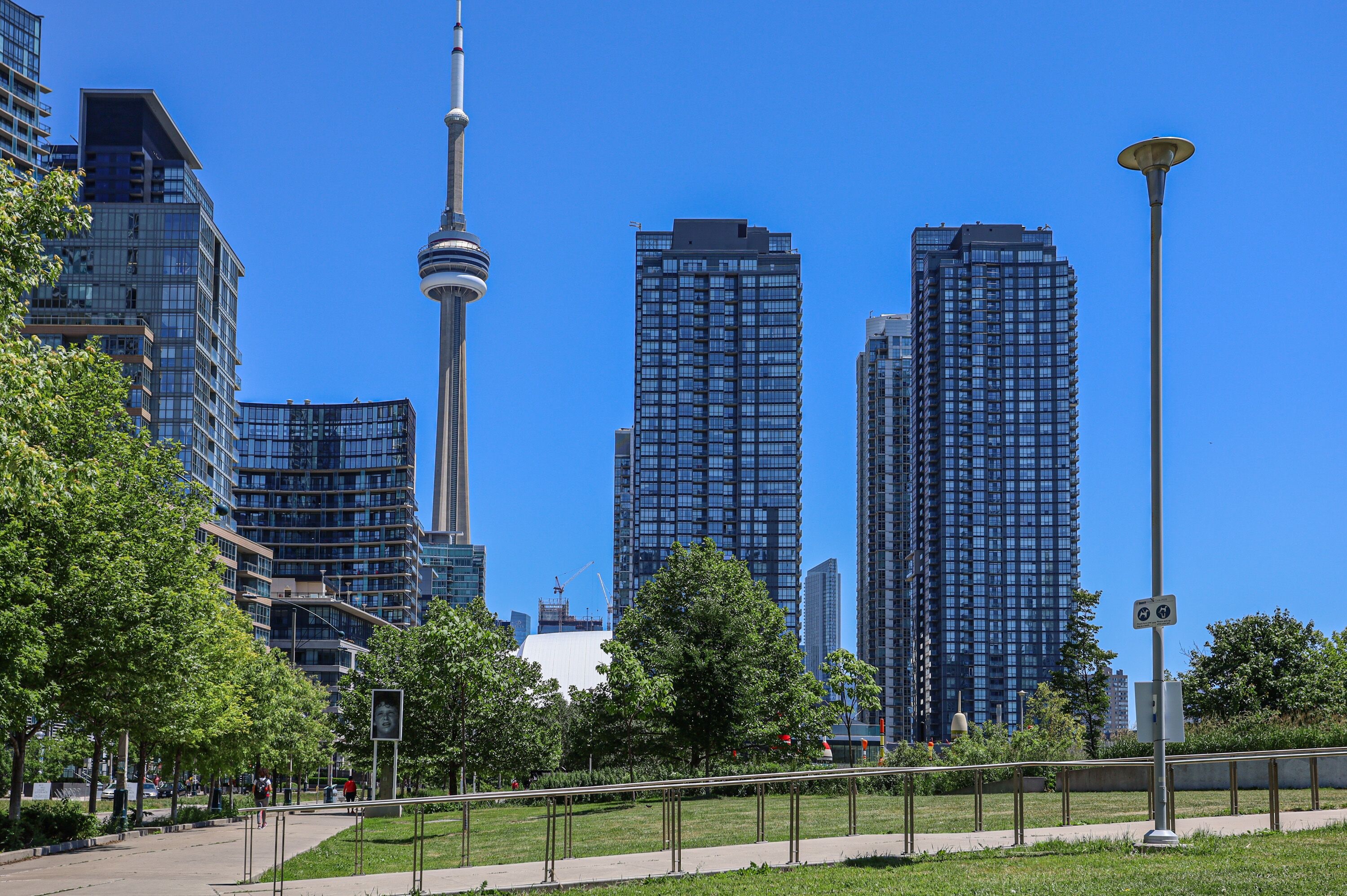 Paisagem urbana com edifícios modernos altos, uma torre imponente e uma área de parque com caminhos e vegetação.