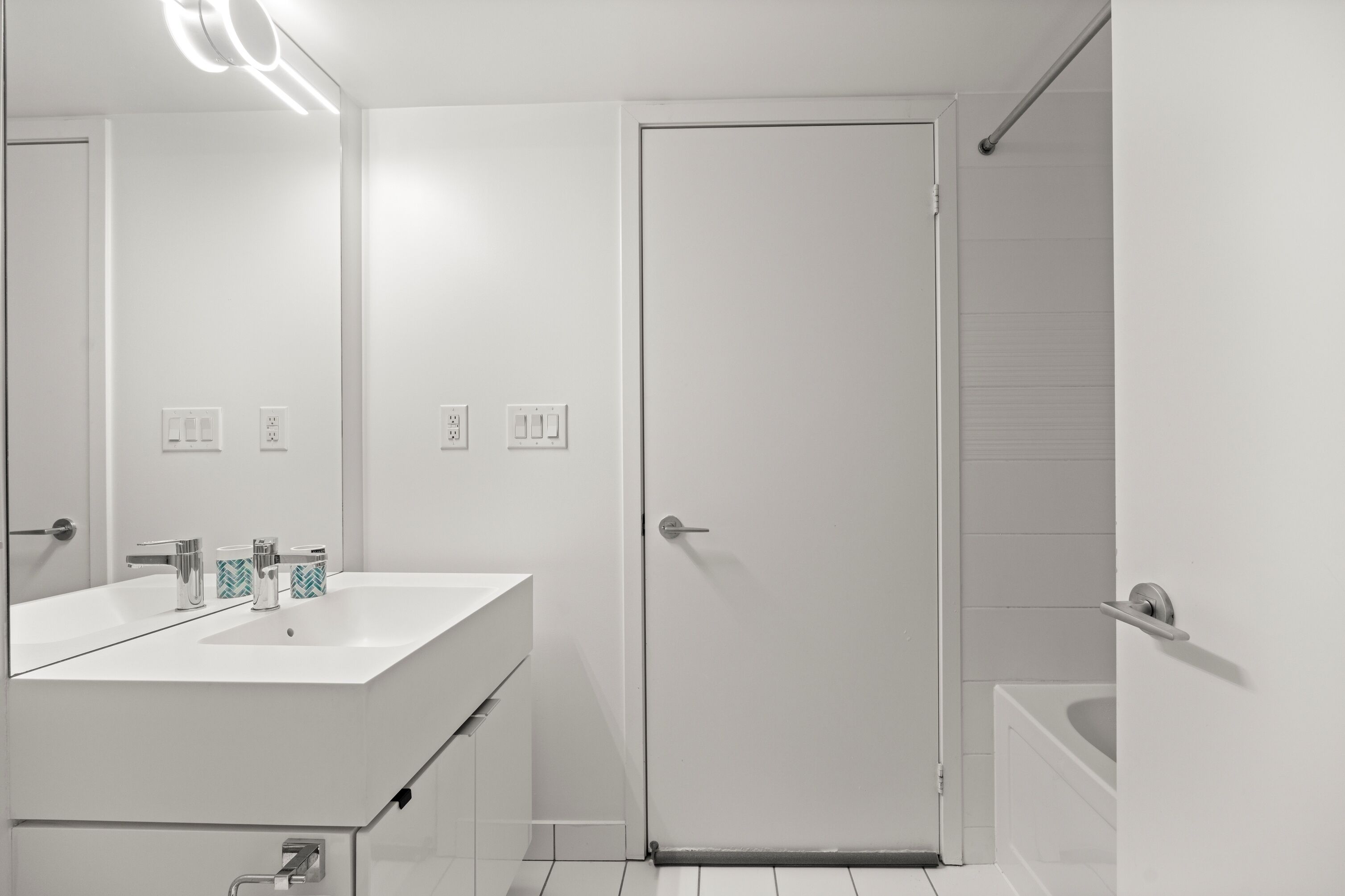 Ein modernes Badezimmer mit Waschbecken, Spiegel und Tür, alles in Weiß.