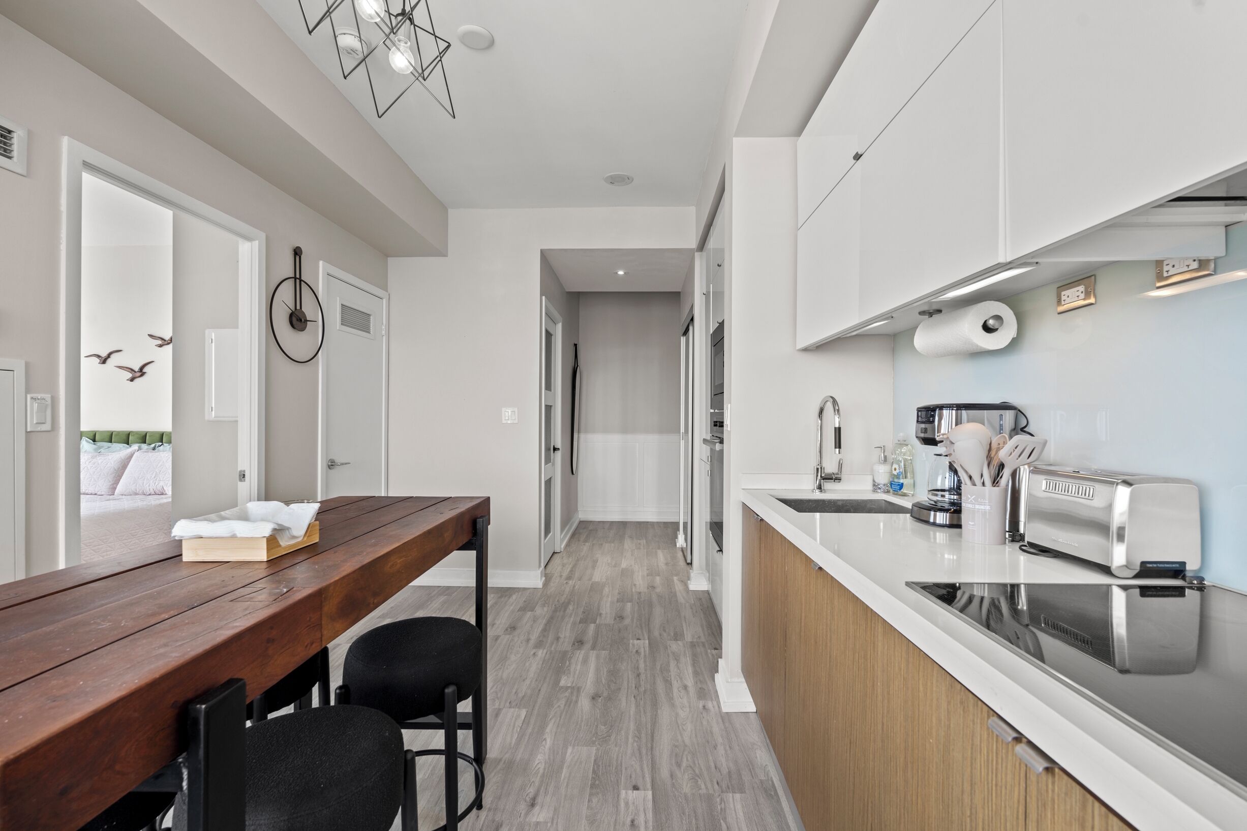 A modern kitchen with white cabinets, a wooden dining table, and a built-in oven.
