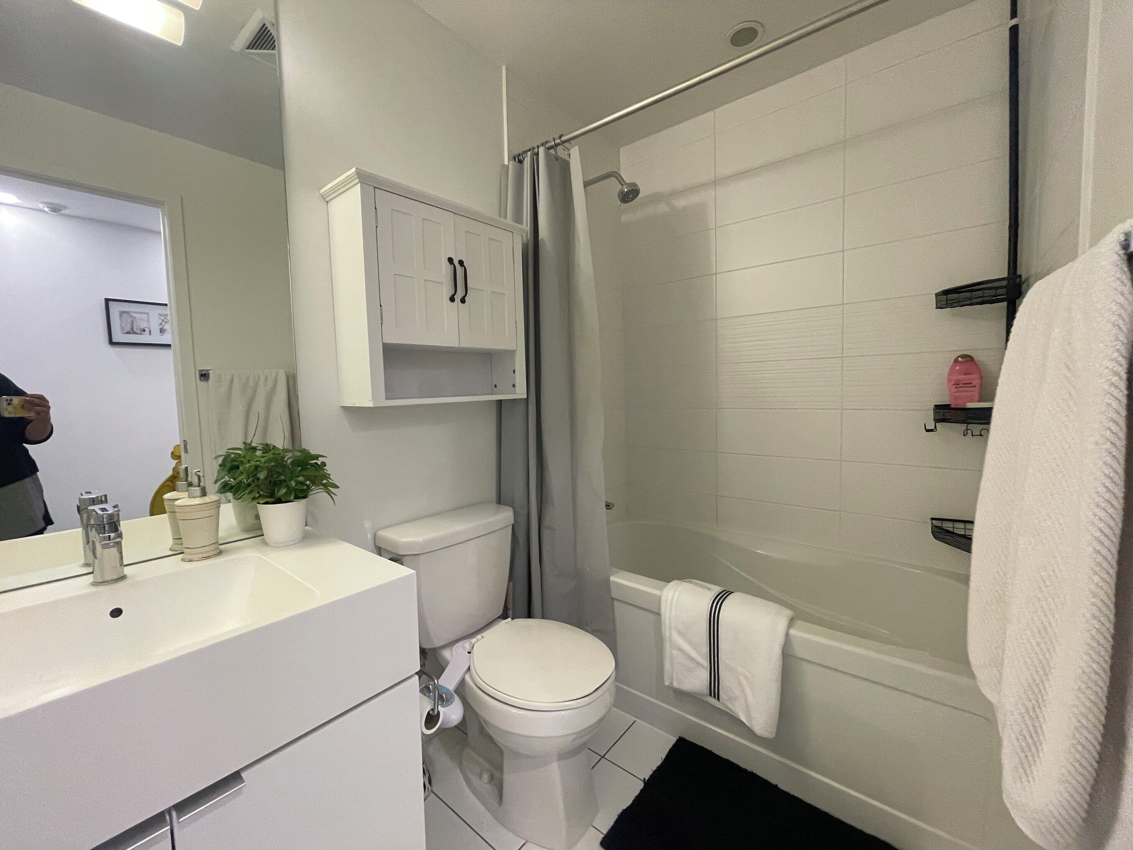 A bathroom with a white sink, toilet, and shower. There is a cabinet above the sink and a towel rack on the wall.
