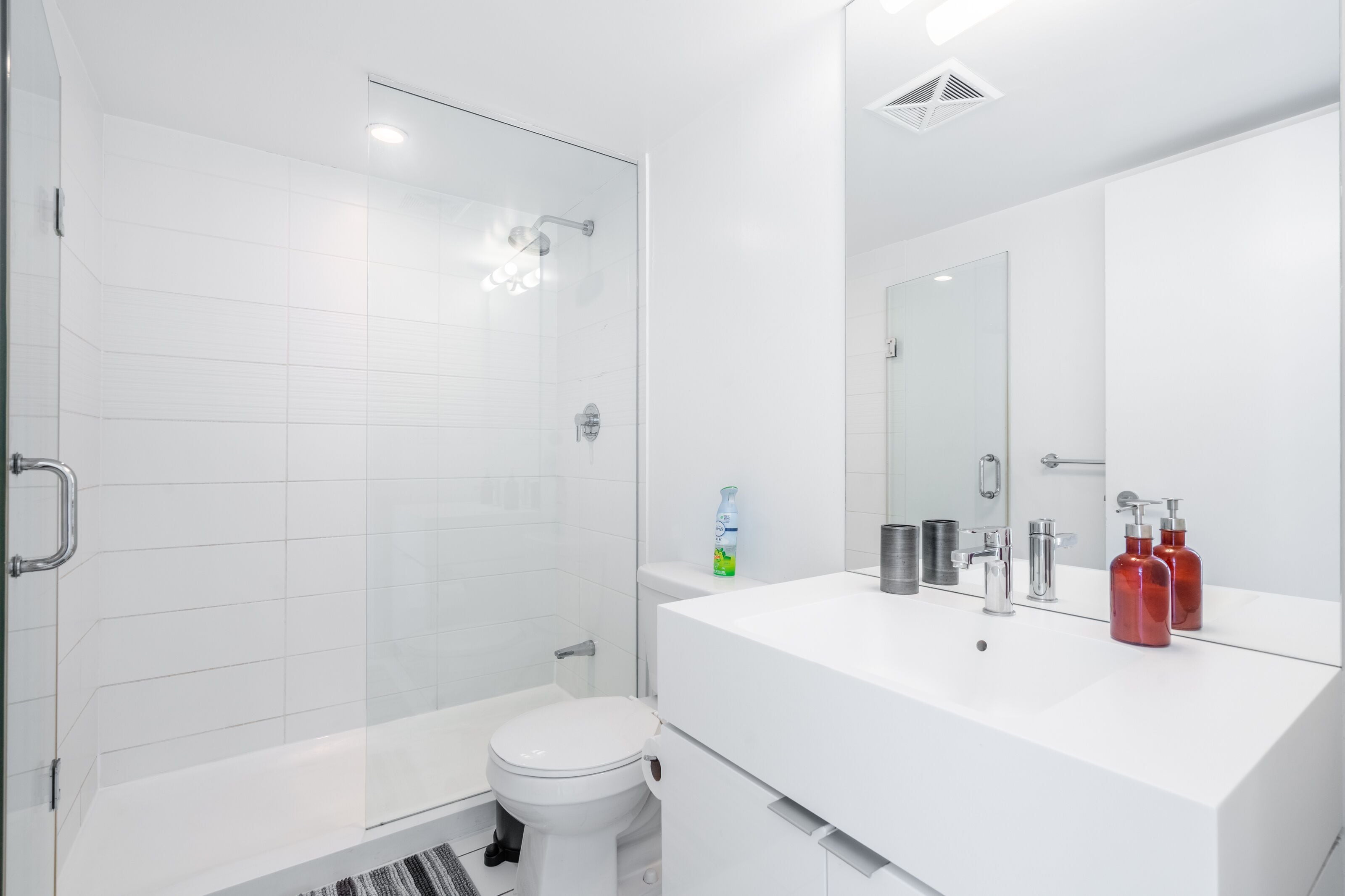 Um banheiro moderno com box de vidro, vaso sanitário branco e toucador com espelho.
