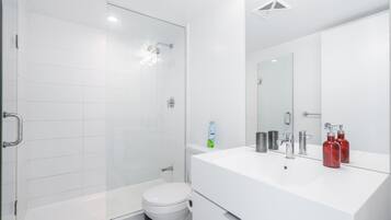 Um banheiro moderno com box de vidro, vaso sanitário branco e toucador com espelho.