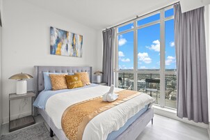 Een moderne slaapkamer met een groot bed en uitzicht op de stad, met een stadslandschap zichtbaar door het raam.