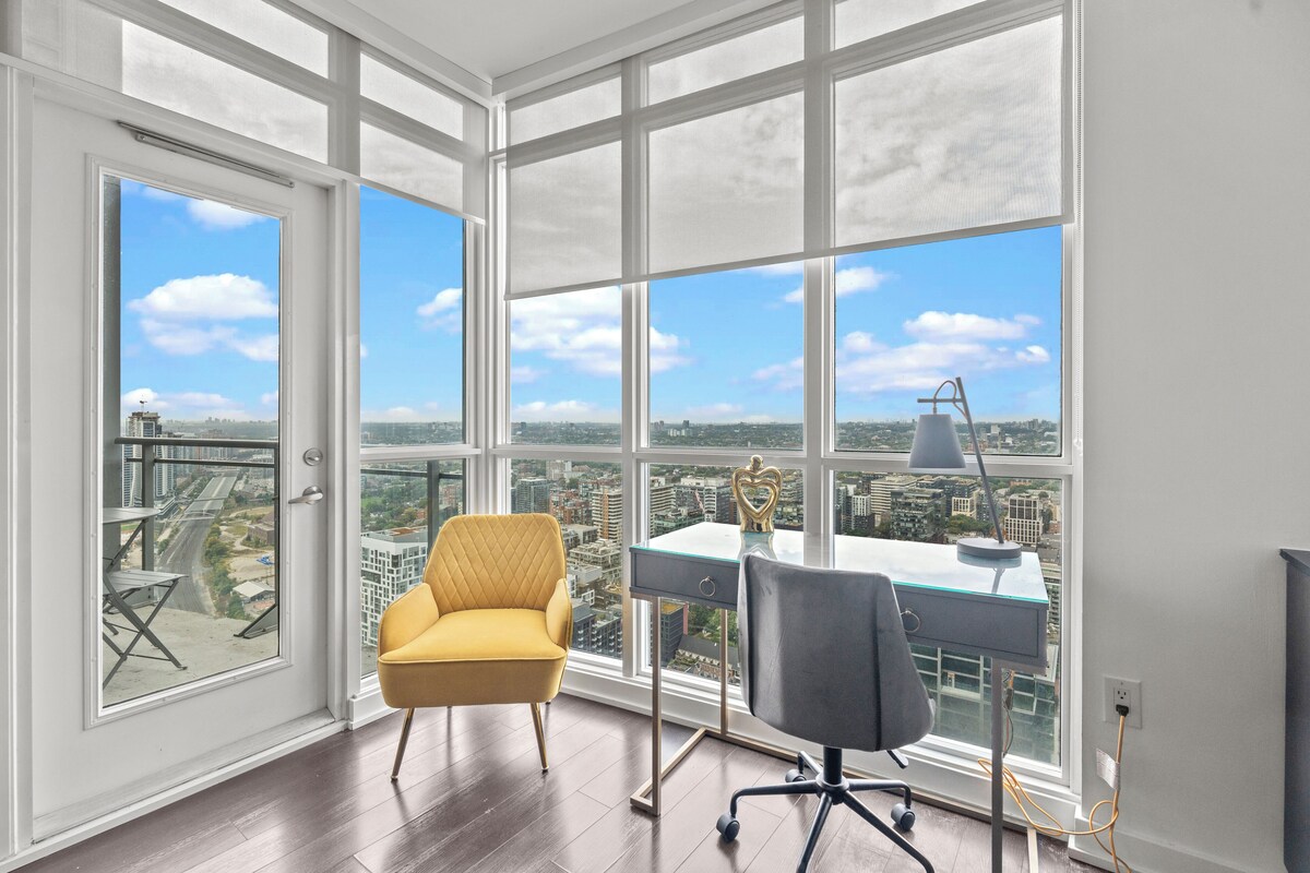 A spacious room with large windows offering a city view, a modern desk, and a comfortable yellow chair.
