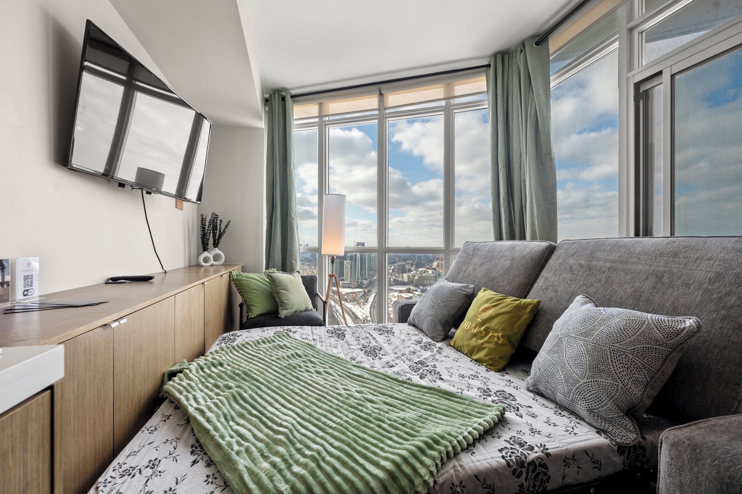 Une chambre d’hôtel moderne équipée d’un lit, d’un canapé, d’un bureau et d’une grande fenêtre donnant sur la ville.