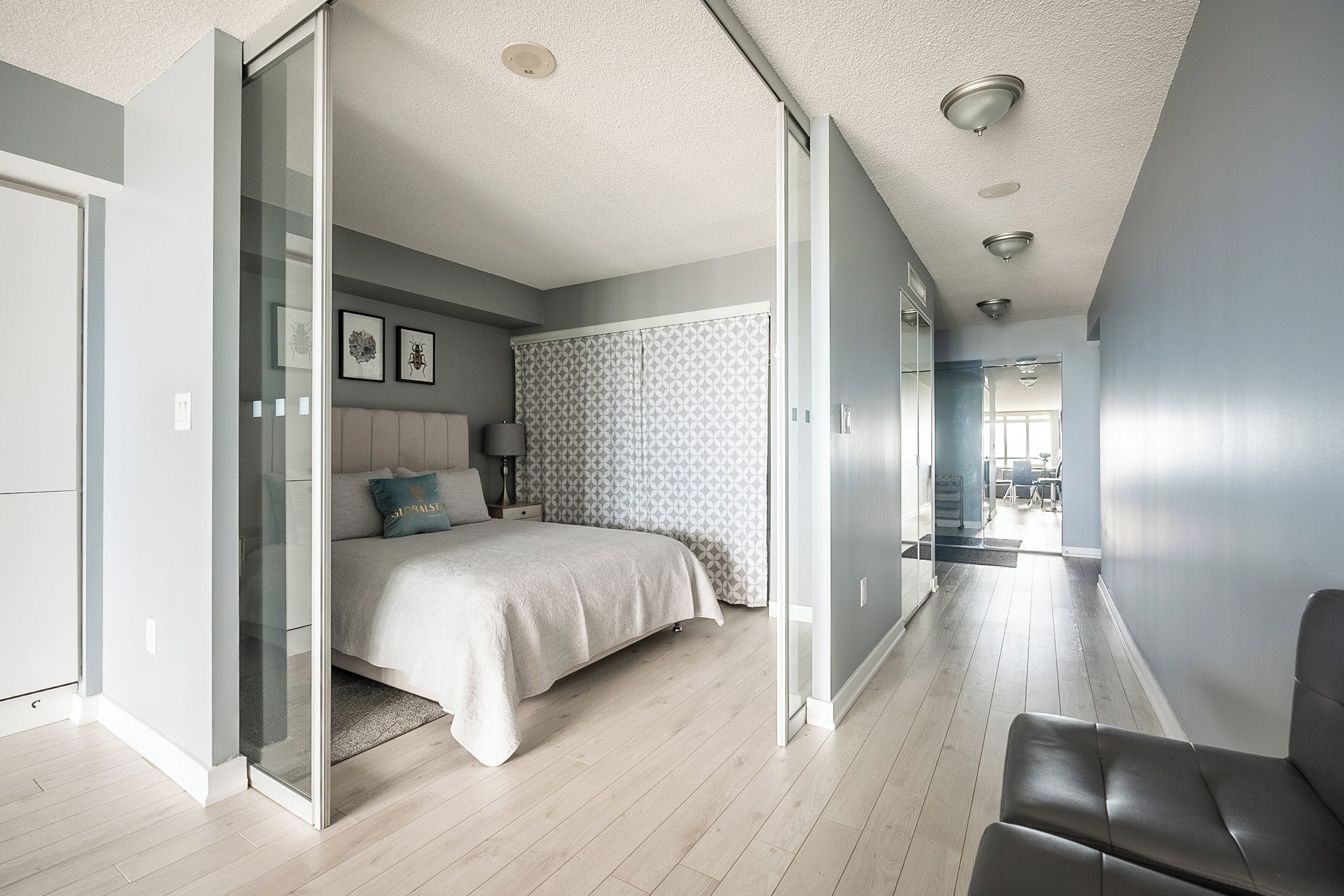 Een moderne slaapkamer met een bed, nachtkastje en een bijzettafeltje. Er is een schuifdeur die naar een andere kamer leidt.