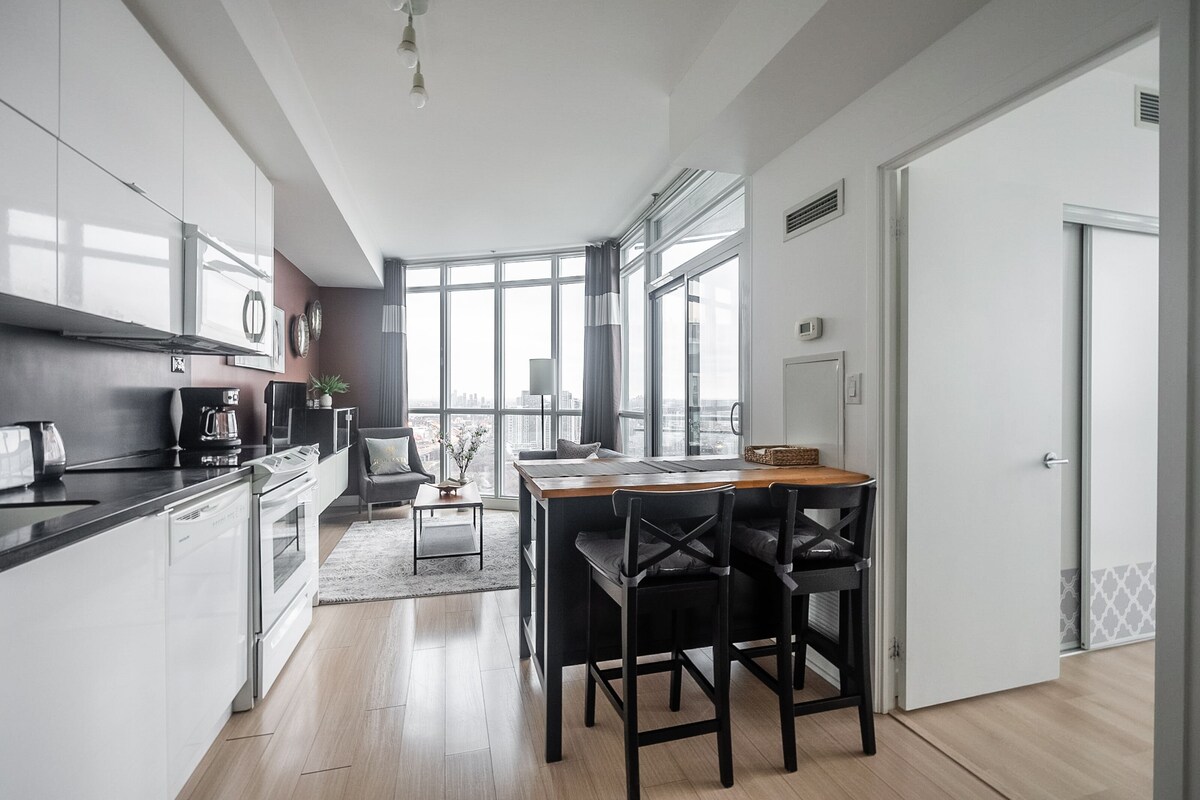 A modern kitchen with a dining area, large windows, and a view of the city.