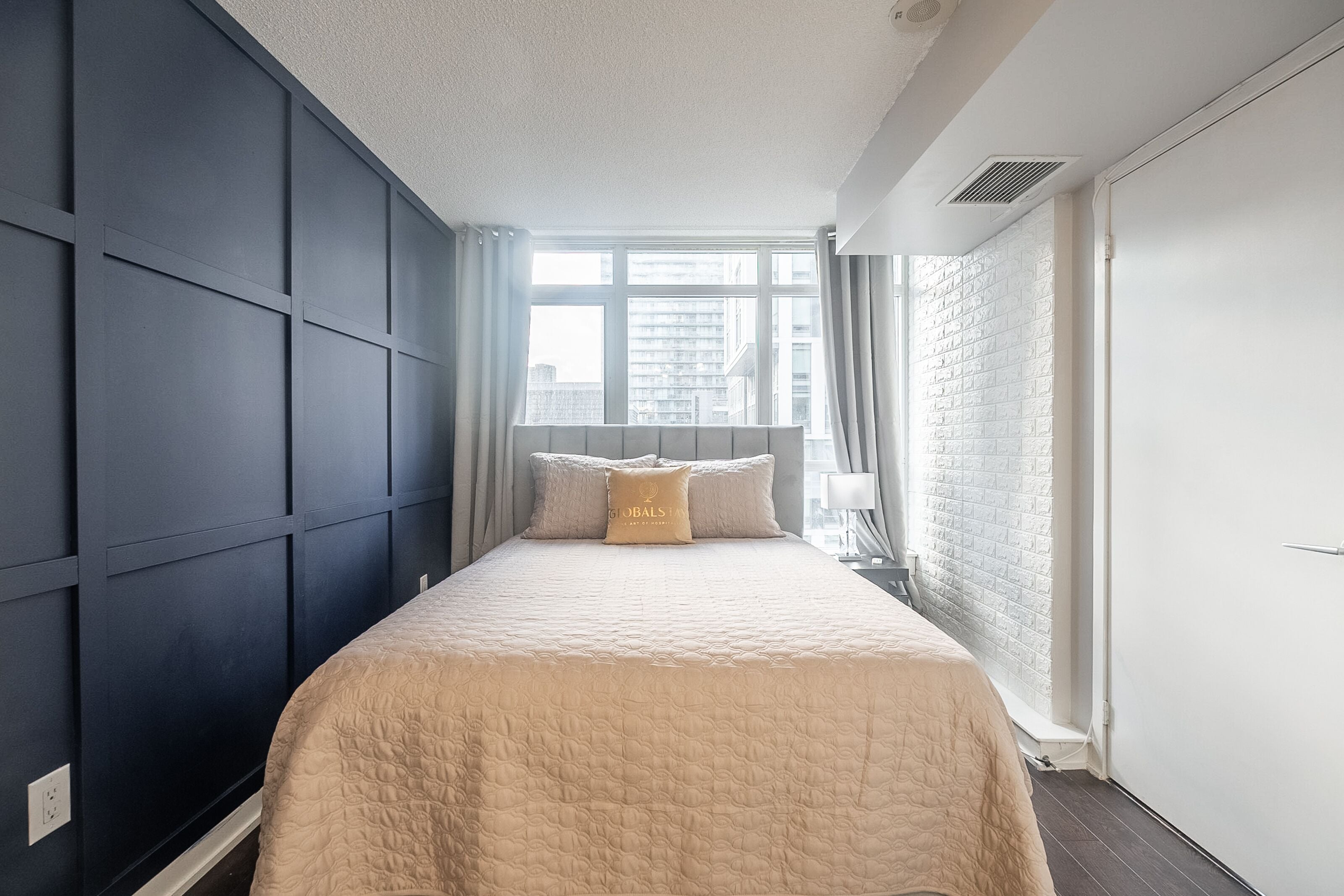 A bedroom with a large bed, a window with curtains, a white brick wall, and a white door.