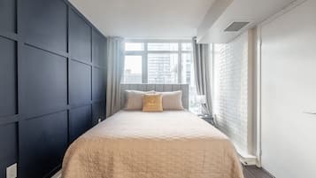 A bedroom with a large bed, a window with curtains, a white brick wall, and a white door.