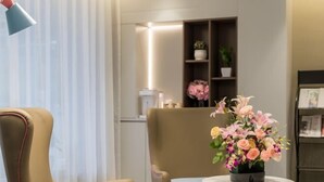A modern living room with a beige armchair, a round coffee table with a floral centerpiece, and a bookshelf in the background. - Home Inn Neo (Shanghai Xujiahui Wanping South Road) (Shanghai)