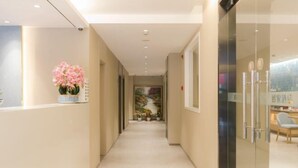 A corridor with a reception desk, a vase of pink flowers, and a glass door leading to a room with a chair and a desk. - Home Inn Neo (Shanghai Xujiahui Wanping South Road) (Shanghai)