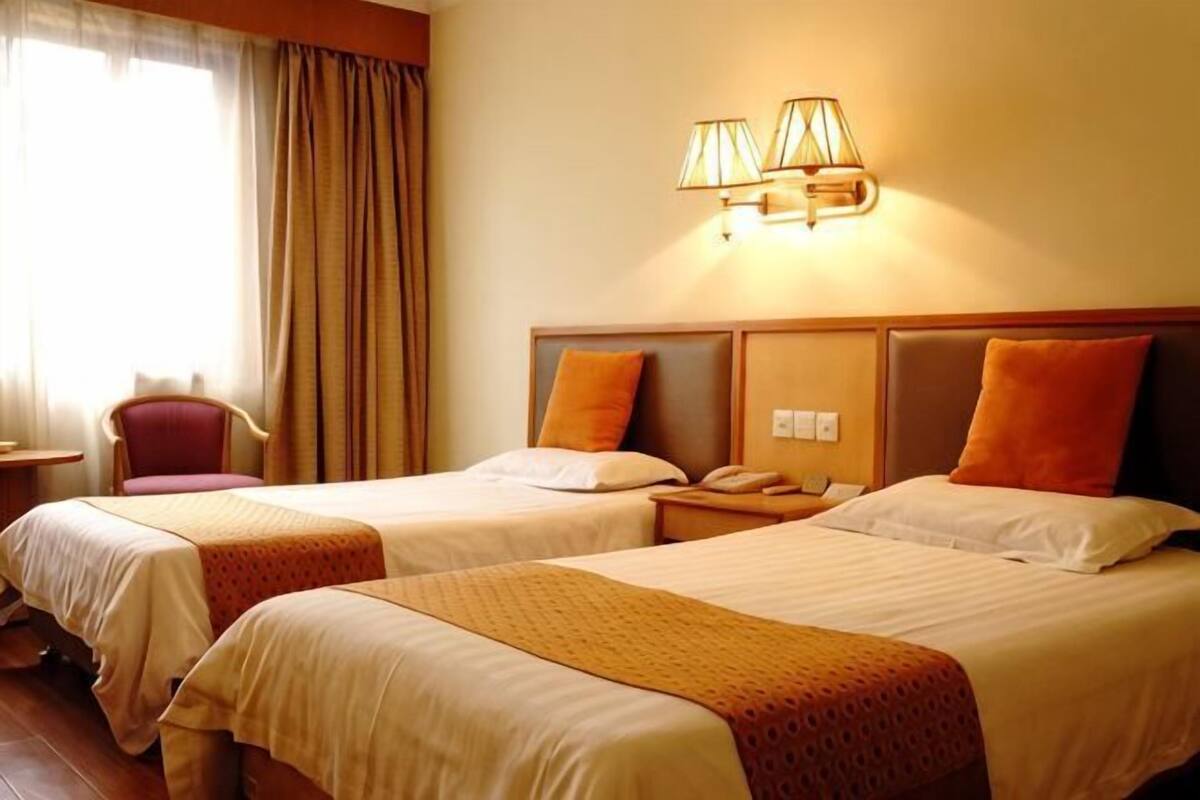 A hotel room with two beds, a desk, a chair, and a lamp.