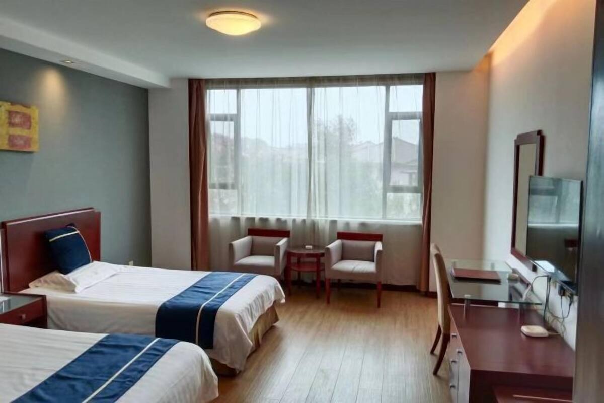 A hotel room with two beds, a desk, a chair, a small table, and a window with curtains.