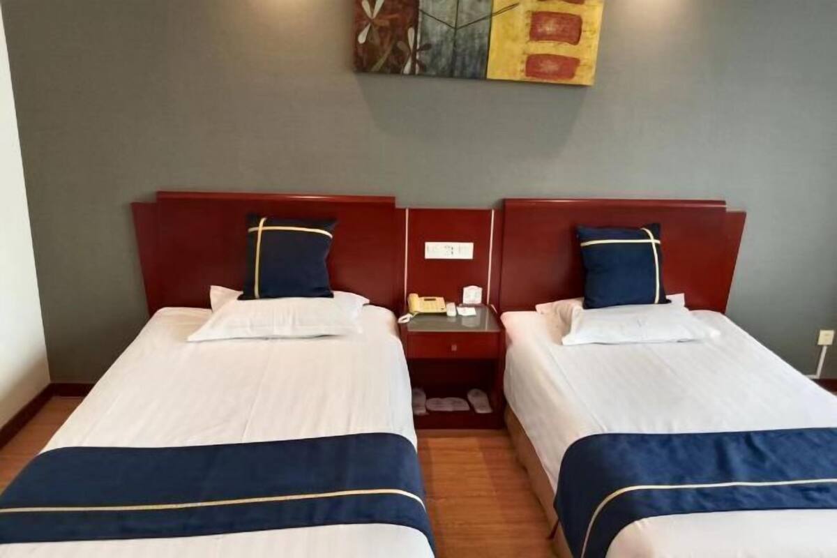 A hotel room with two beds, each with a white and blue bedspread, a red headboard, and a small bedside table with a phone and a lamp.