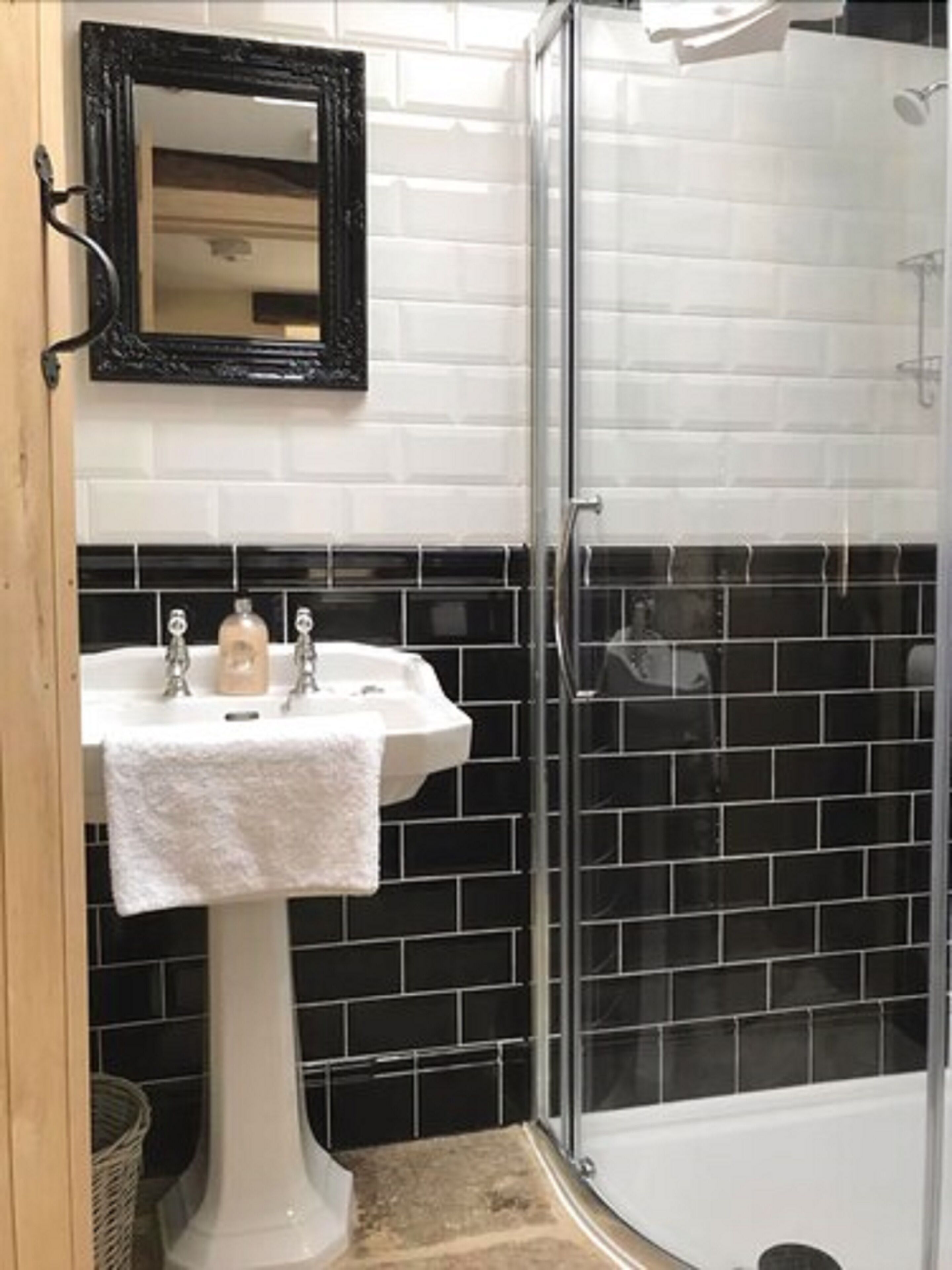 A bathroom with a white pedestal sink, black tiled walls, and a glass shower enclosure.
