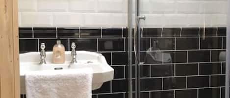 A bathroom with a white pedestal sink, black tiled walls, and a glass shower enclosure.