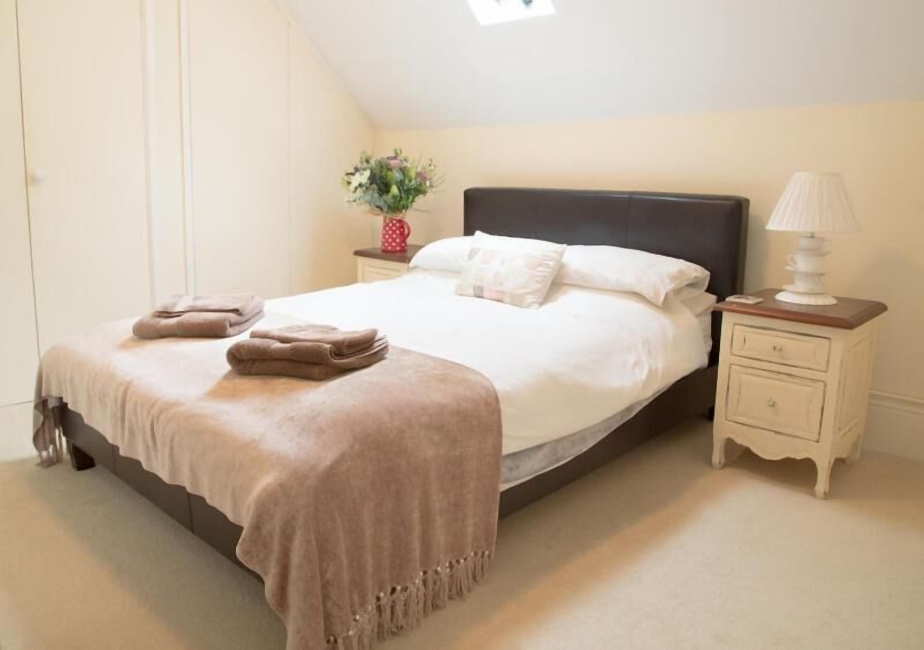 A bedroom with a bed, a nightstand, a lamp, and a vase with flowers.