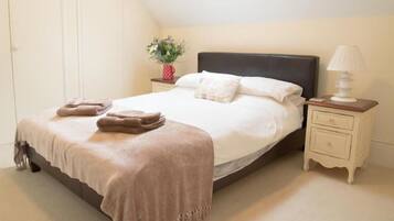 A bedroom with a bed, a nightstand, a lamp, and a vase with flowers.
