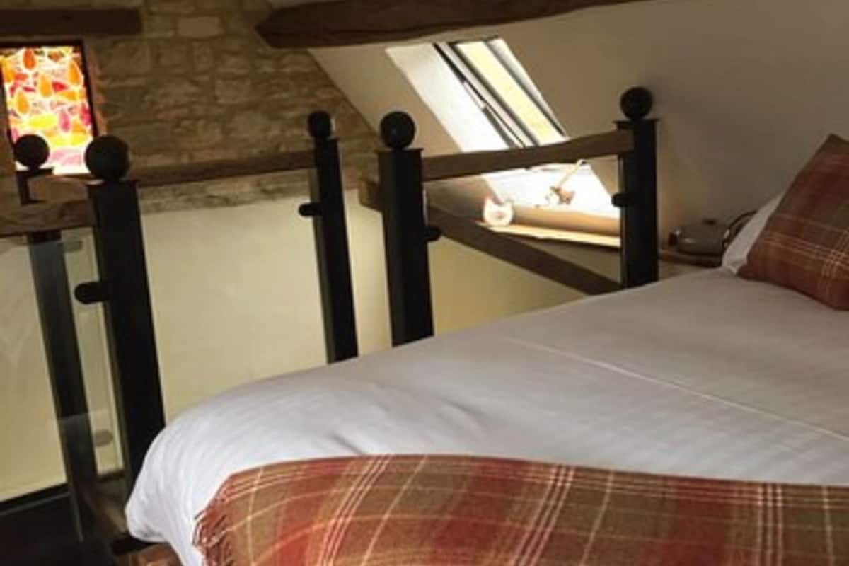 A bedroom with a sloped ceiling, a wooden bed frame, a plaid blanket, and a stone wall.