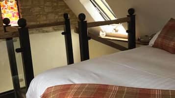 Un dormitorio con techo inclinado, estructura de cama de madera, manta escocesa y pared de piedra.