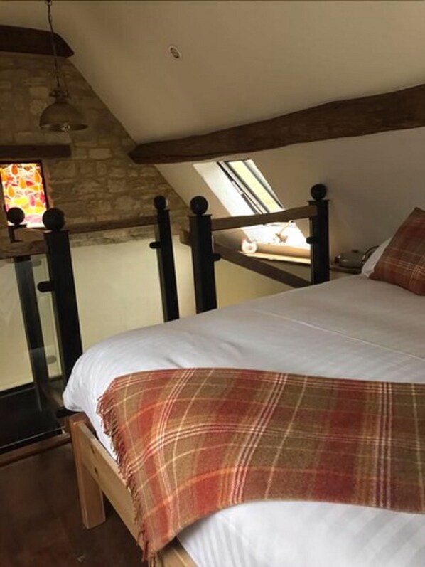 A bedroom with a sloped ceiling, a wooden bed frame, a plaid blanket, and a stone wall. - The Bantam Tea Rooms & Guest House (Chipping Campden)