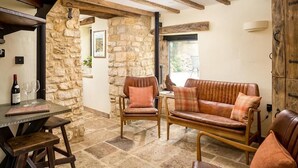 Un intérieur rustique avec des murs en pierre, des poutres en bois, une cheminée en pierre, des canapés en cuir et une table à manger agrémentée de verres à vin.