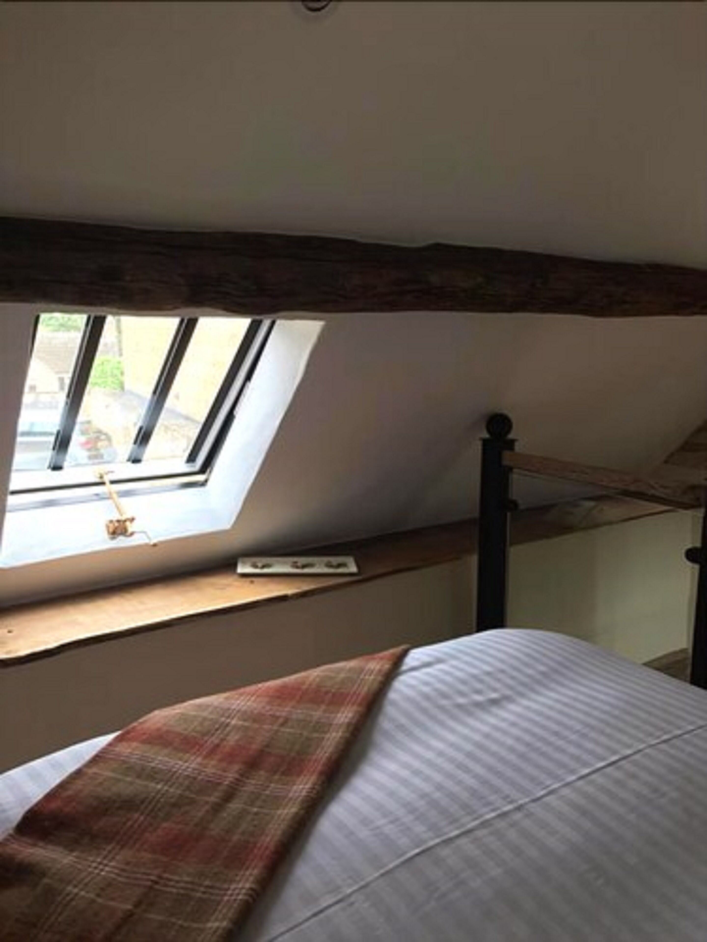 A bedroom with a skylight, a bed, and a wooden headboard.