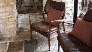 Une pièce aux murs de pierre, avec une chaise et un canapé en bois, un sol en pierre et une vue sur un coin cuisine.