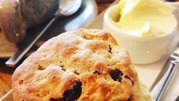Un muffin à la croûte friable et contenant des morceaux de fruits visibles, servi avec un petit ramequin de beurre et une tasse de café sur un plateau.