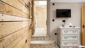 Une pièce comprenant une armoire en bois, une commode blanche, un téléviseur et un espace douche.