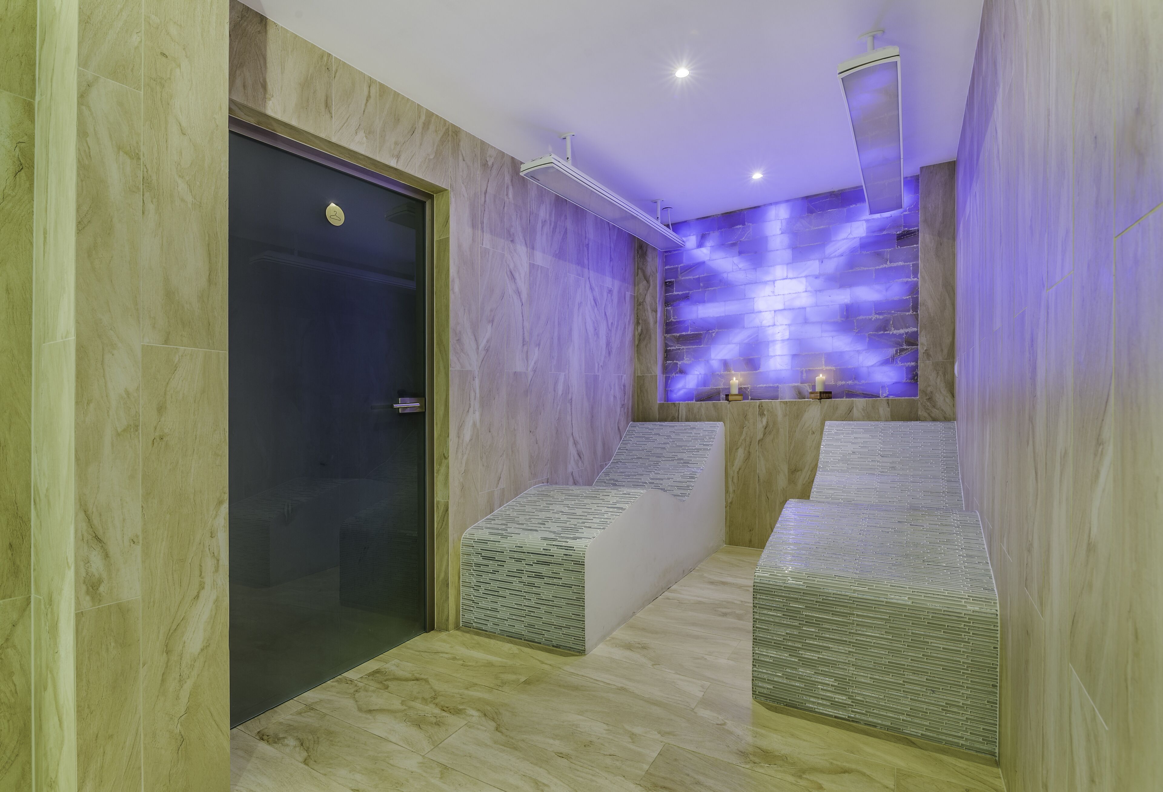 A modern bathroom with marble walls, a glass door, and a purple-lit wall feature.